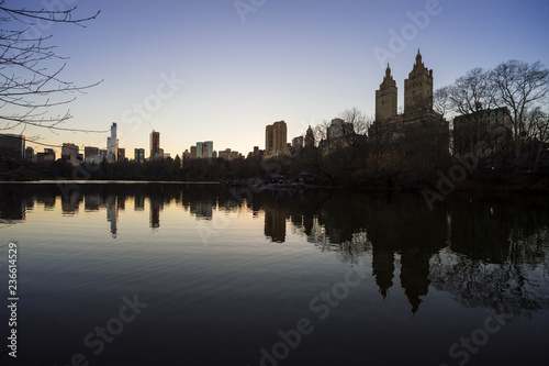 Tranquil sunset view of the scenic skyline silhouette of the Upper West Side reflecting on the flat surface of the Central Park Lake on a calm winter evening in New York City