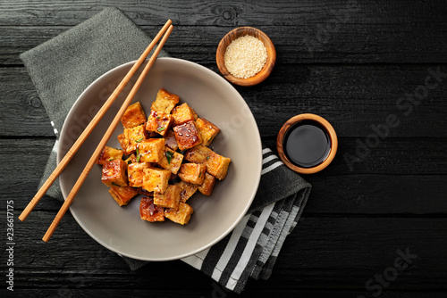 Fried tofu with sesame seeds and spices on black background.