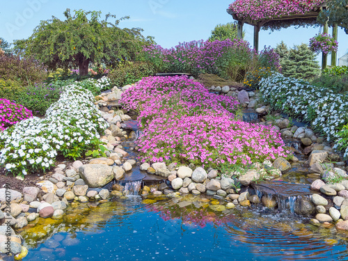 water pool in ornamental rock garden with waterfalls and pink petunias and white impatiens