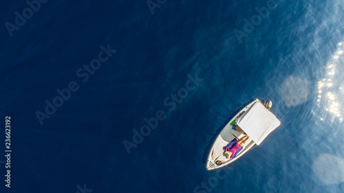 Top view of a white boat sailing in the blue sea. Young woman in pink lying with large hat in relax.