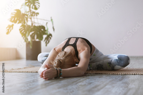 Close-up attractive sporty young woman practicing yoga indoor on wooden floor on bamboo mat. Beautiful fitness girl doing yoga asana in class. Healthy lifestyle, calmness, relax photo