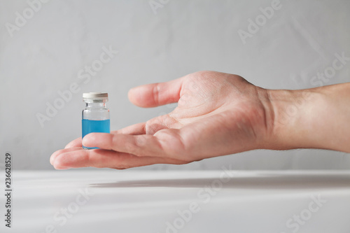Human hand holding an old glass vial filled with cyan blue liquid on white blurred background