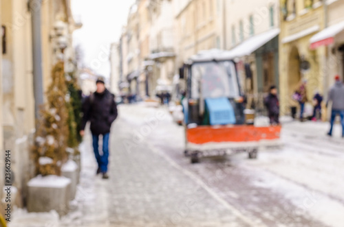 Blurred winter background city snow cleaner technician tractor removes snow communal services life bad weather lifestyle blizzard christmas cold falls snow tourists panorama old city © mykytivoandr