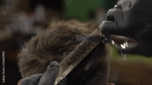 Male hands dressed in black gloves is cutting short hair of the client with the help of comb in a barbershop photo