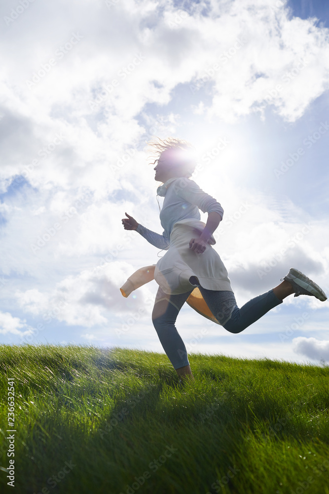 Active young woman running against skyline and sun shining among clouds on sky Active young woman running against skyline and sun shining among clouds on sky