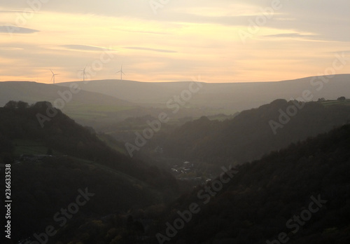 a soft hillside tree covered valley landscape blurred by fog at sunrise glowing a warm orange color with the tops of hills showing though the mist