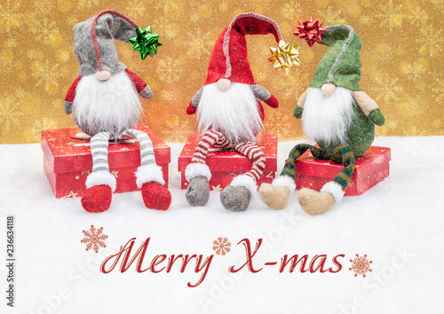 Weihnachtliche Grußkarte, Wichtel mit Zipfelmützen sitzen auf Geschenken im Schnee mit goldenen Schneeflocken im Hintergrund.