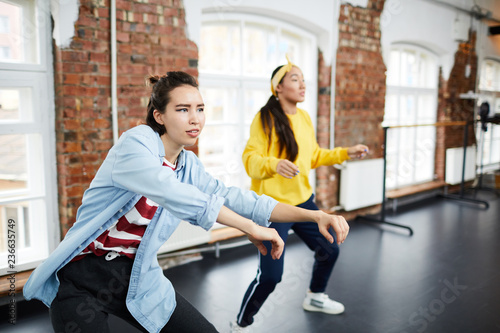Young active woman and her groupmate learning hip hop dancing in modern studio