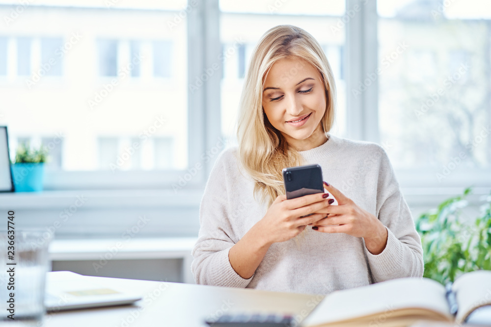Smiling woman using smartphone while working in home office Smiling woman using smartphone while working in home office