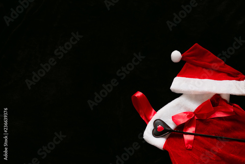BDSM background. Dark background with red Santa dress and whip in the corner. Message space for Christmas and New Year. Winter flat lay with copy space.