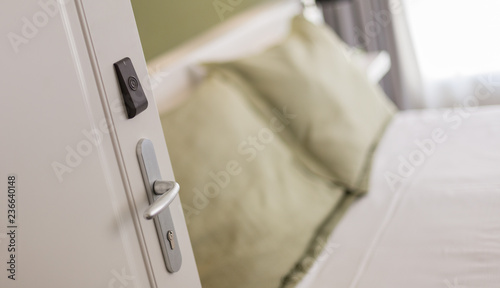 White open door with electronic lock in a hotel room with double bed 