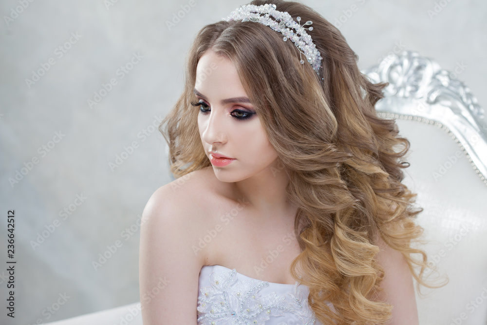 Charming young bride with luxury hairstyle. Beautiful woman in wedding dress sitting in a chair.