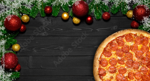 Pizza pepperoni Christmas snowflake with fir branches and new year toy ball,  on black wood board table photo