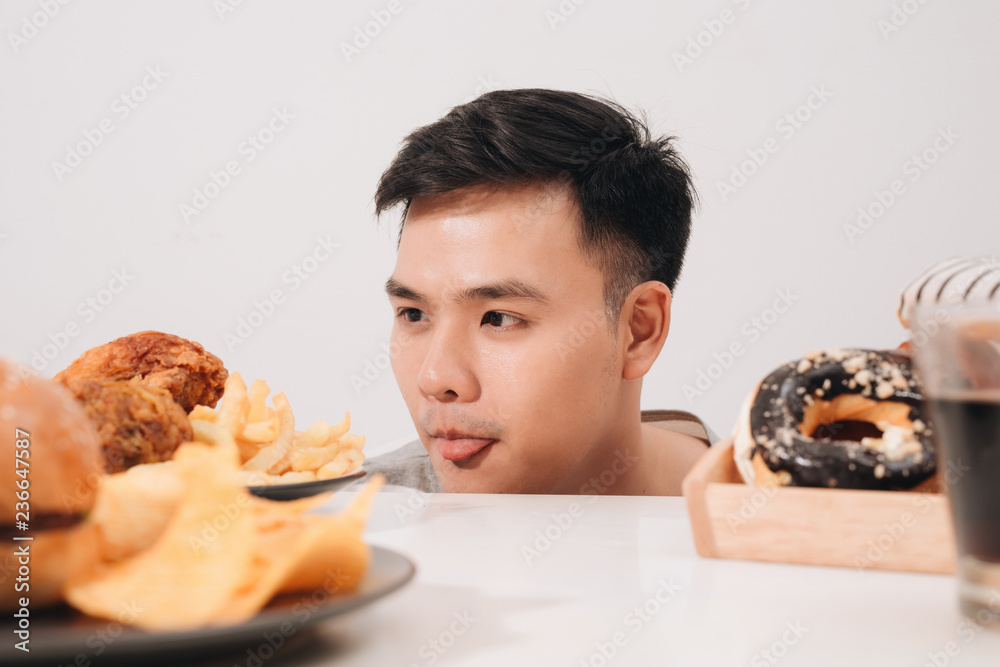 Young man having cravings for donuts, hamburger, chicken with fries instead Young man having cravings for donuts, hamburger, chicken with fries instead
