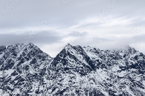 Rocky mountains in snow and cloudy gray sky at winter