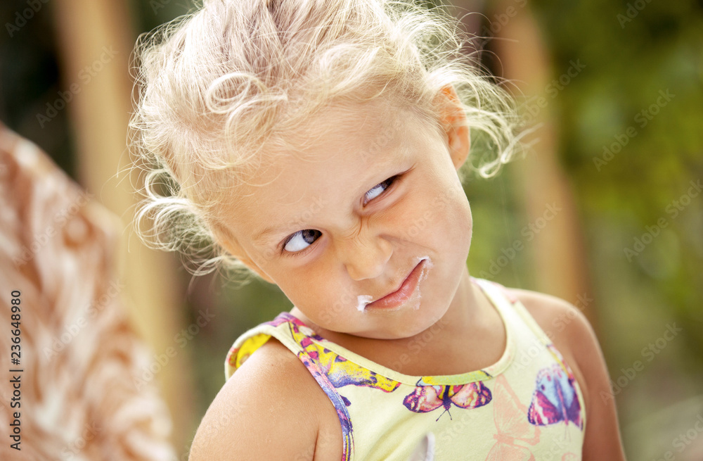 Cute girl child with yogurt marks on her face on a colorful background. Unique emotions close-up Cute girl child with yogurt marks on her face on a colorful background. Unique emotions close-up