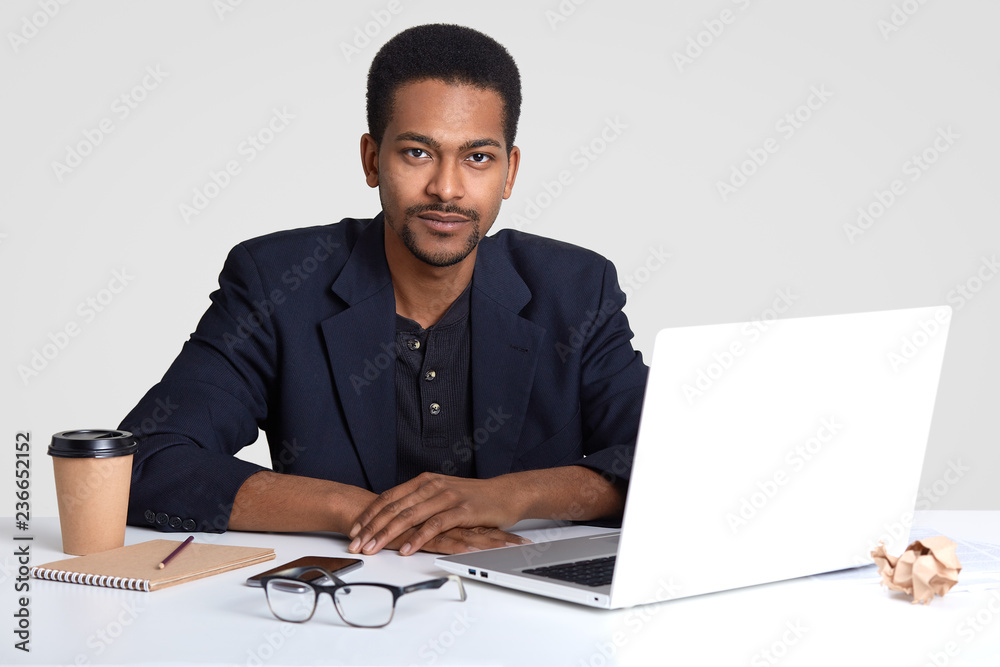 Image of serious male employee with self confident expression, dressed in formal clothing, works freelance, prepares project work on portable laptop computer, isolated over white studio wall Image of serious male employee with self confident expression, dressed in formal clothing, works freelance, prepares project work on portable laptop computer, isolated over white studio wall
