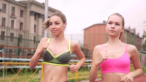 Two young women running in a summer stadium. One in headphones listens to music.