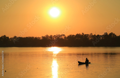 Silhouette of a fisherman working on his boat at the lake before sunset 