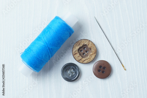 Blue threads, buttons and a needle on a white table
