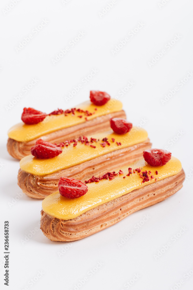 Set of delicious eclairs with yellow glaze and raspberries Set of delicious eclairs with yellow glaze and raspberries