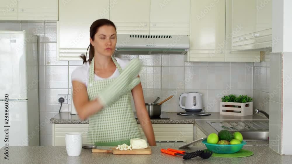 Young woman in apron dancing silly on kitchen with mitten. Funny female enjoying herself moving ridiculously while preparing meal Young woman in apron dancing silly on kitchen with mitten. Funny female enjoying herself moving ridiculously while preparing meal