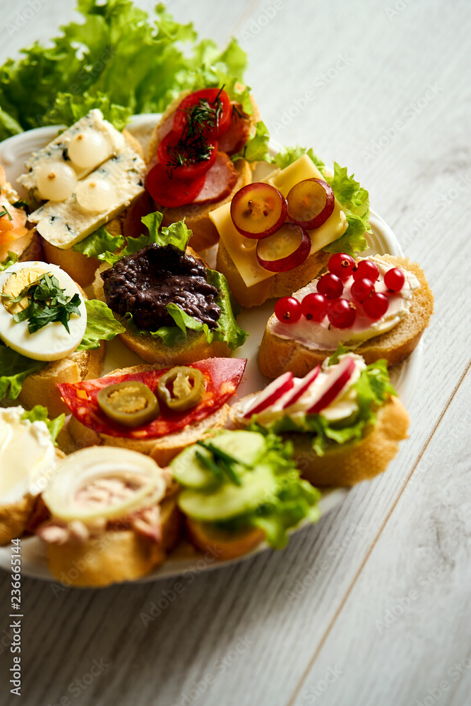 plate with colorful and healthy sandwiches or tapas on a light wooden table