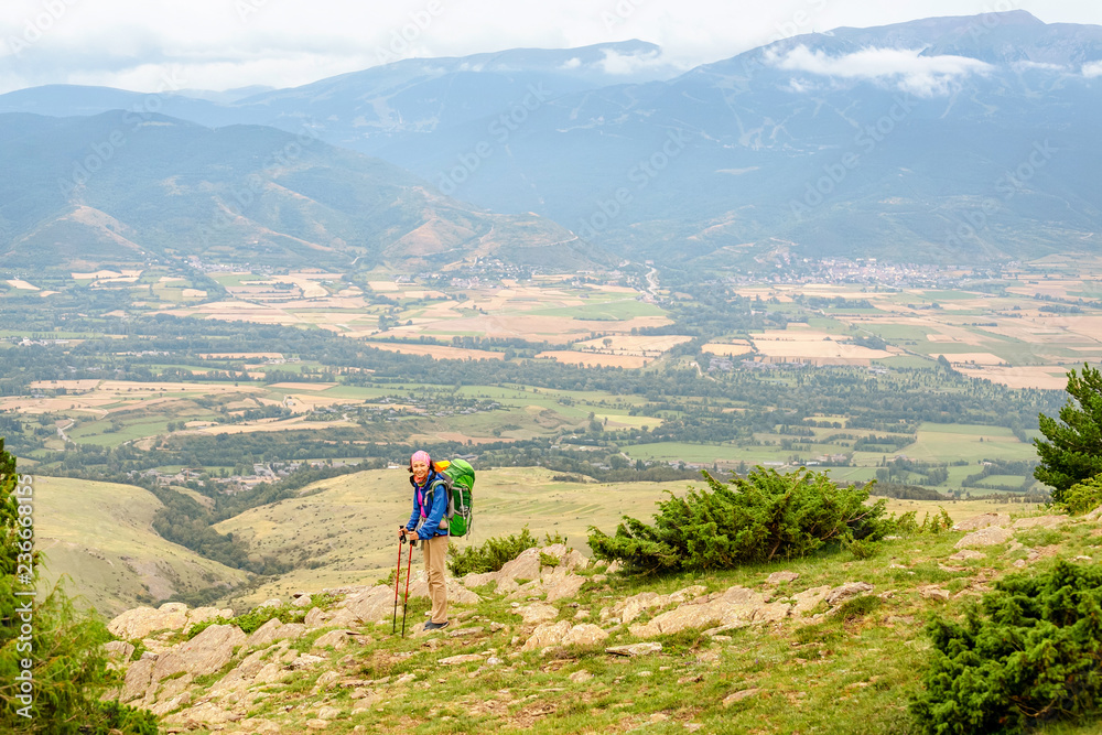 Woman hiker with big backpack stands on the rock and enjoys the valley view in Spanish Pyrenees mountains