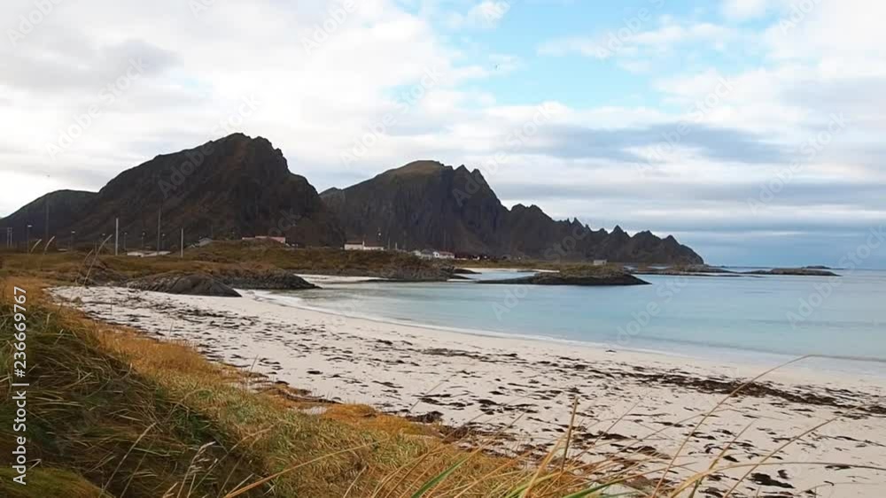 Blue ocean with mountain and rocks on a white sandy beach in Norway