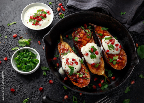 Grilled eggplants with yogurt sauce, pomegranate seeds, parsley and green onion in cast iron vintage pan.