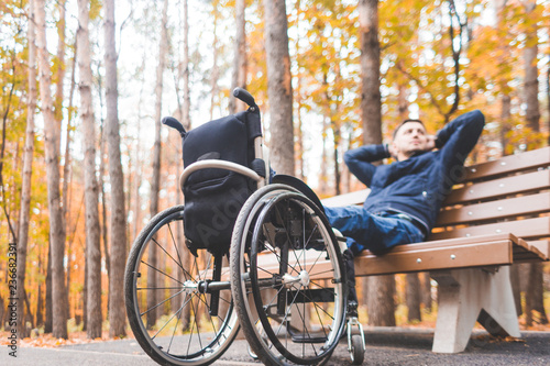 Young man resting sitting on a bench with his legs on his wheelchair.