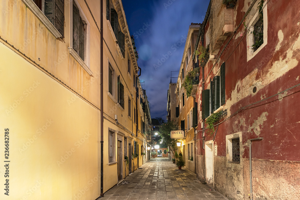 A narrow street with apartments and a hotel signboard iluminated at night, Venice, Italy.