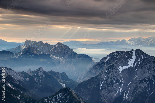 Sun rays burst through dark grey cloud cover over misty jagged Koschutnikturm Kosutnikov Turn peaks of Koschuta Kosuta ridge in Karawanken Karavanke range in autumn morning, Austria / Slovenia Europe photo