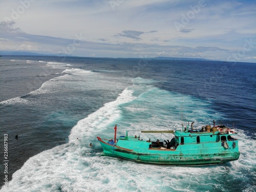 Canvas Print Green tucker boat stranded near the beach with waves passing underneath and arou