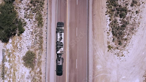 Top view drone zooming in on white truck going by camera on beautiful highway road in the middle of sandstone desert.