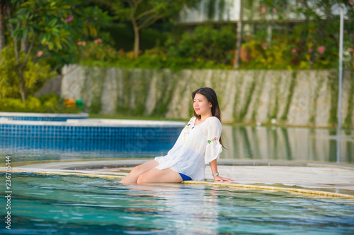 outdoors lifestyle portrait of young happy and beautiful Asian Korean tourist woman relaxing at tropical resort swimming pool enjoying Summer holidays smiling cheerful