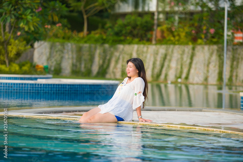 outdoors lifestyle portrait of young happy and beautiful Asian Chinese tourist woman relaxing at tropical resort swimming pool enjoying Summer holidays smiling cheerful