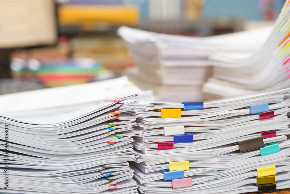 Pile of unfinished document on office desk. Stack of homework assignment archive with colorful paper clip and binder clip on teacher table waiting to be managed. Education and business concept. Pile of unfinished document on office desk. Stack of homework assignment archive with colorful paper clip and binder clip on teacher table waiting to be managed. Education and business concept.
