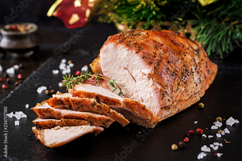 Roasted sliced Christmas ham of turkey on dark rustic background. Festival food.