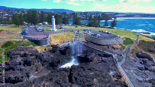 Amazing aerial footage of the kiama blowhole spouting water with the lighthouse in the backdrop. photo