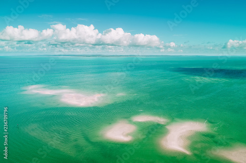 Aerial view of fluffy clouds over vivid turquoise shallow ocean water and patches of sand