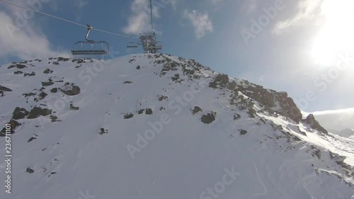 Point of view, a ski lift going up on top of the mountain with view of rocks and mountain on a sunny day and leaving the ski chair lift, 50 fps photo