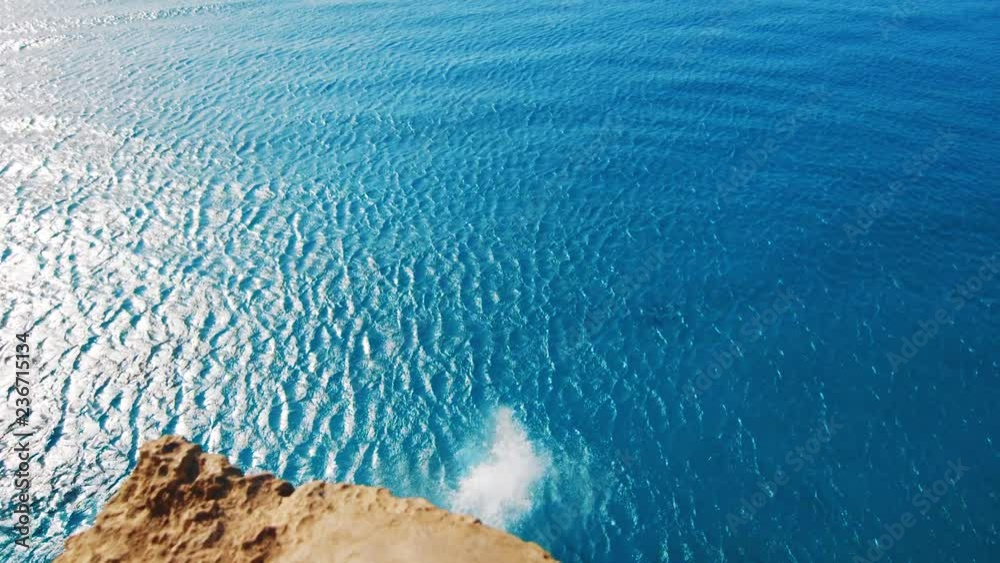 Girl jumping off cliff into blue Caribbean Sea, Slow Motion view from Behind