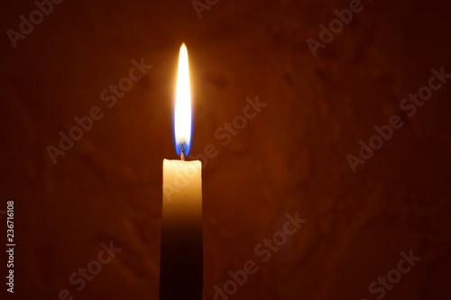 One yellow candle flame burning on dark red blurred background with copy space for text. Advent or memorial prayer candle flame.