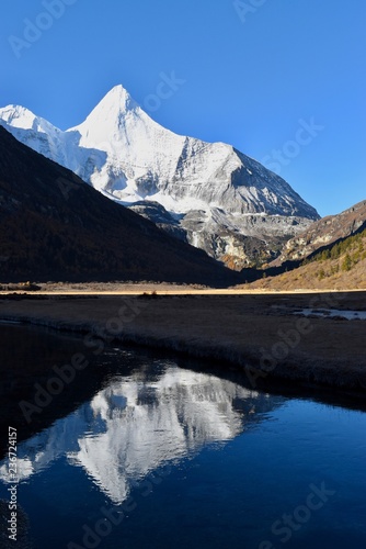 Sacred mountain Jambeyang (5,958m) with blue sky background and its reflection on icy clean lake. This place is supposed to be the real Shangrila. Daocheng Yading Nature Reserve, Sichuan, China.  photo