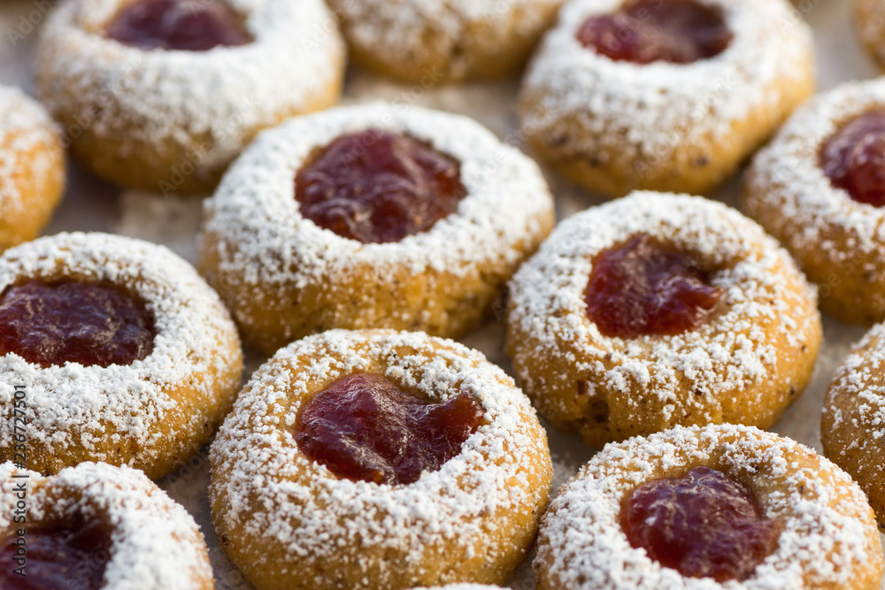 Christmas shortbread thumbprint cookies with strawberry jam powdered with castor sugar on white parchment paper on baking tray. Top view close up. Festive atmosphere. Holiday pastry baking