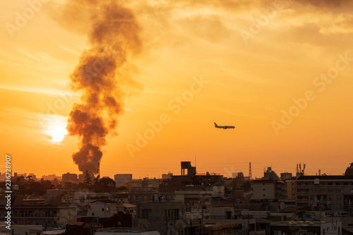 Osaka, Japan - December 2, 2018: Plane comes in for landing at Itami Airport as smoke from building fire plumes into setting sun