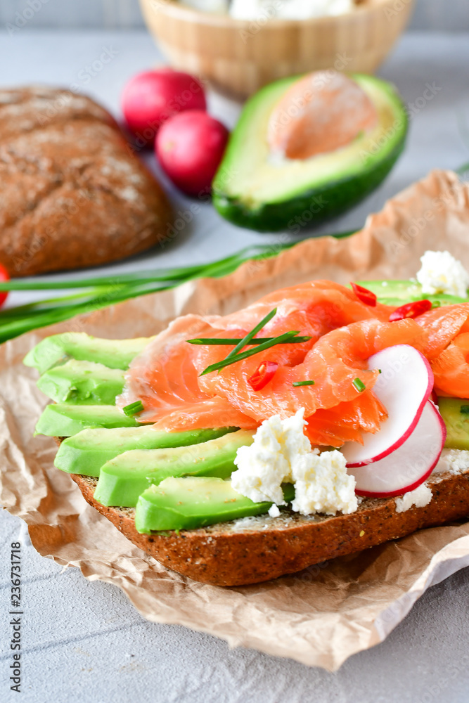 sandwich with avocado and salmon on a light background, green onions and gluten-free grain bread, radishes and tomatoes. concept diet food, copy space, sandwich take away, healthy fast food sandwich with avocado and salmon on a light background, green onions and gluten-free grain bread, radishes and tomatoes. concept diet food, copy space, sandwich take away, healthy fast food