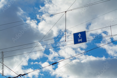 Many street wires stretched in the city against the sky with a sign of a dedicated line for public transport