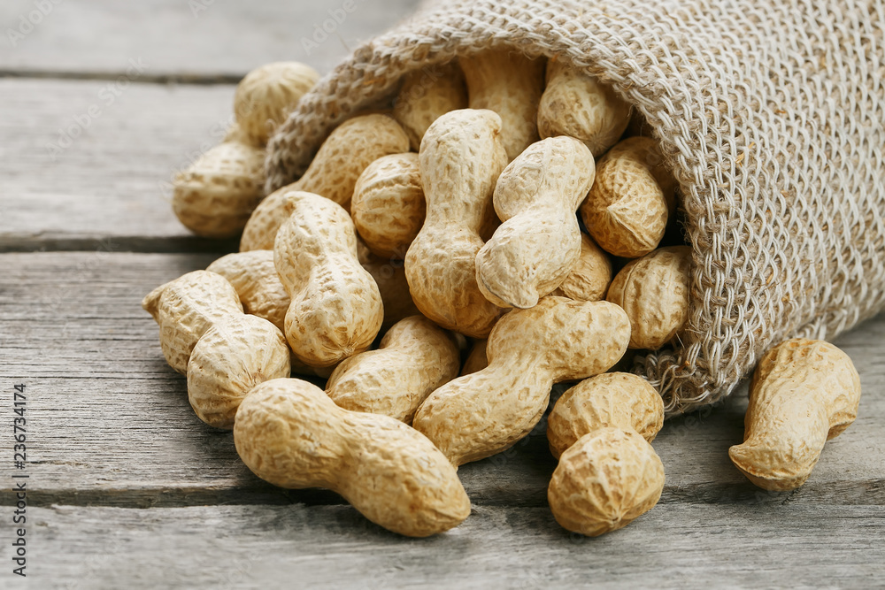 Peanuts in a miniature burlap bag on old, gray wooden surface
